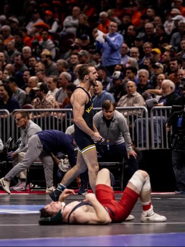 Wrestler celebrates victory while opponent lies on the mat.