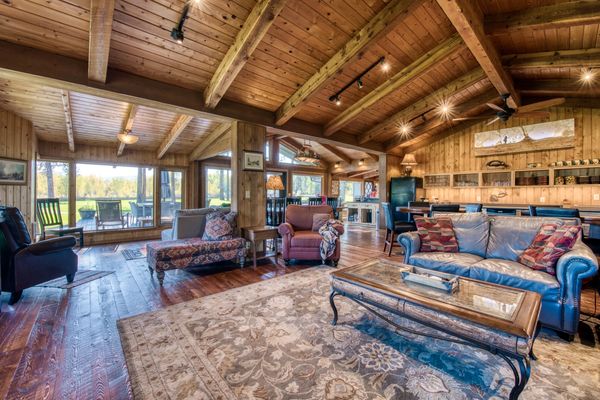 Rustic living room with wooden beams, cozy seating, and large windows overlooking a green landscape.