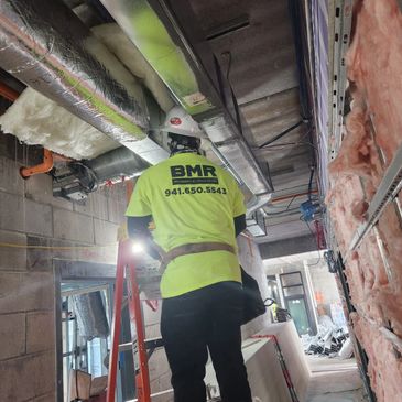Construction worker on ladder inspecting HVAC ducts at building site.