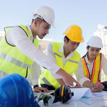 Three construction workers reviewing plans at a site, wearing safety gear.