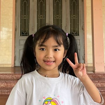 A smiling girl with pigtails showing a peace sign.