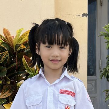 Young girl in school uniform smiling outdoors.