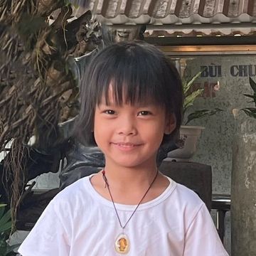 Smiling young child with a necklace in a white shirt.