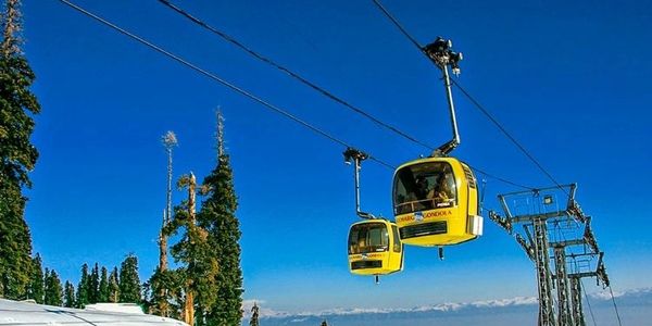 Yellow cable cars gliding over snowy mountain landscape under clear blue sky.