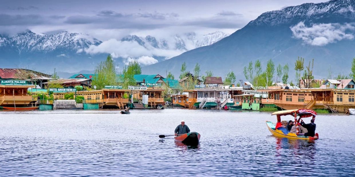 Boats on a serene lake with houseboats and snow-capped mountains in the background.