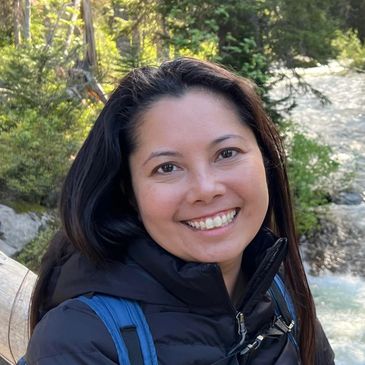 Smiling woman outdoors with a river and trees in the background.