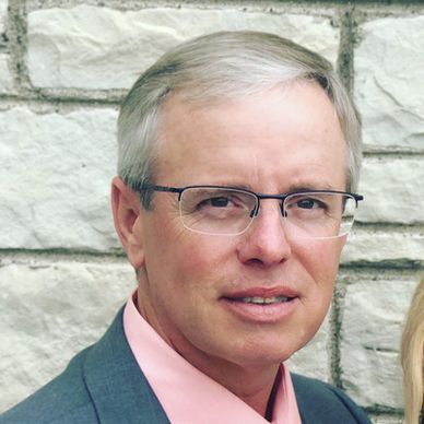 Portrait of a middle-aged man with glasses against a stone wall.