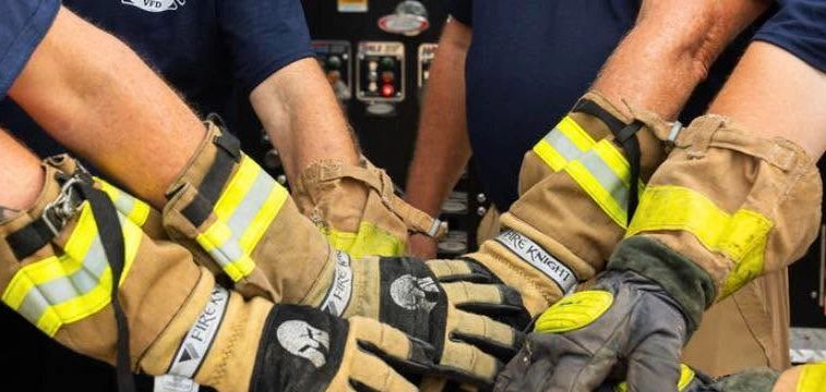 Firefighters join hands wearing protective gloves, symbolizing teamwork and unity.