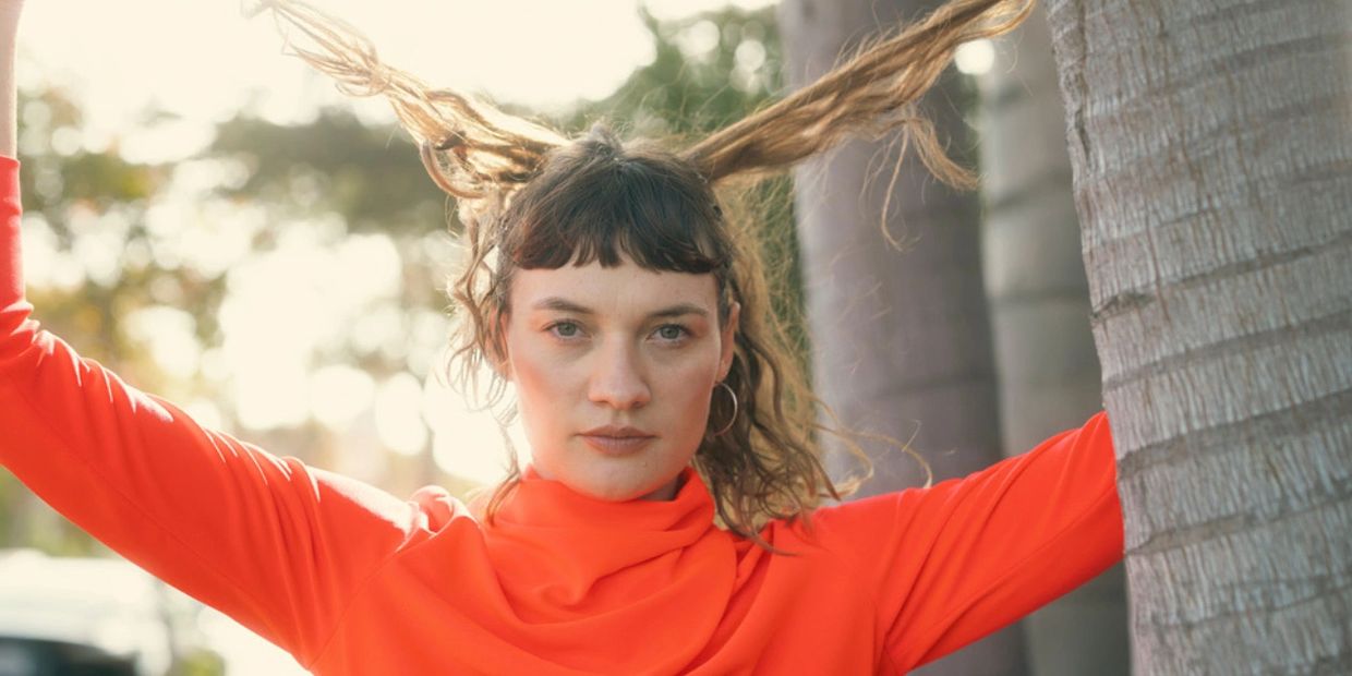Woman in orange sweater holding her hair up outdoors.