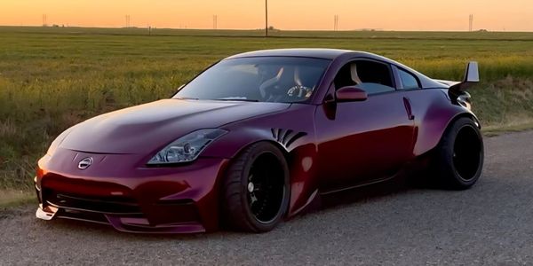 Sleek maroon Nissan sports car with wide body kit and large rear spoiler at sunset.