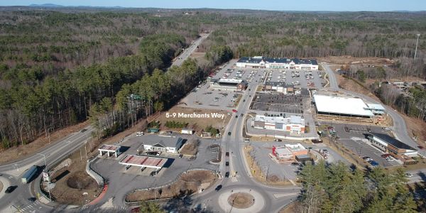 Aerial view of a commercial area with roads, parking lots, and buildings surrounded by trees.