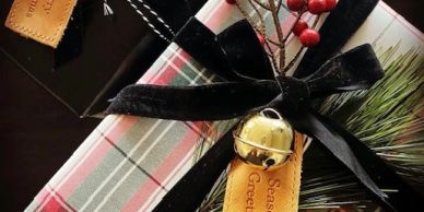 Festive wrapped gift with black velvet ribbon, jingle bell, and holiday tag.