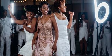 Three women in elegant dresses dancing at a lively party with ring lights.