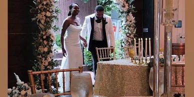 A bride and groom enter a beautifully decorated wedding reception with floral arches.