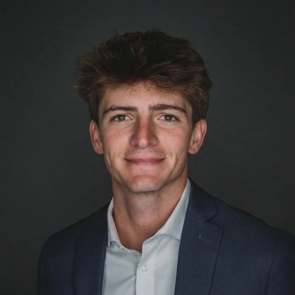 Young man in a suit smiling against a dark background.
