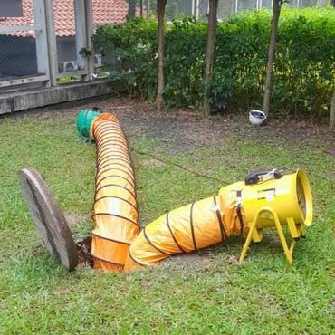 Yellow ventilation ducting extending from a manhole to a blower fan on grass.