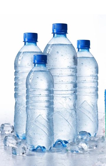 Four plastic water bottles with blue caps surrounded by ice cubes.