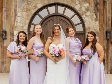 Bride with bridesmaids in lavender dresses posing outdoors.