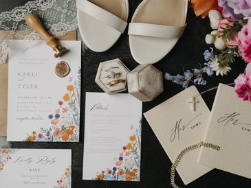 Flat lay of wedding invitations, shoes, rings, and floral decorations.
