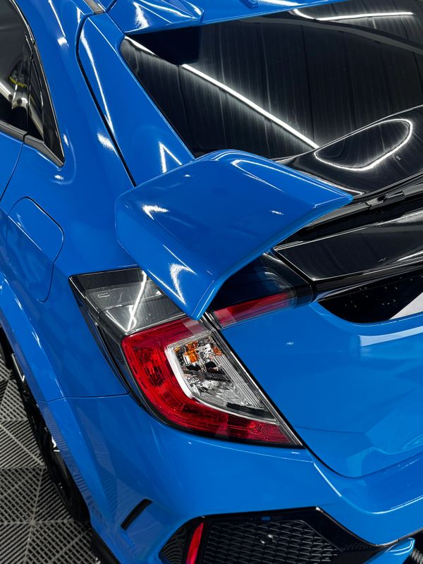 Close-up of a blue sports car's rear spoiler and taillight.
