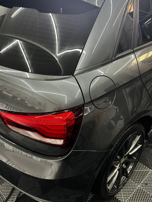 Close-up of a sleek gray car's rear with shiny wheel and red tail light.