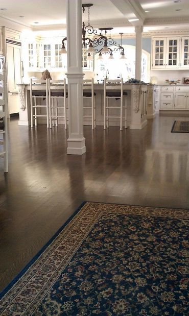 Elegant kitchen with white cabinetry, a large island, and a dark wooden floor accented by a patterned rug.
