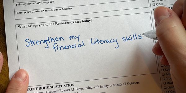 Person writing 'Strengthen my financial literacy skills' on a form.