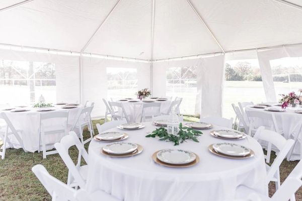 Round tables with white padded chairs under a tent.