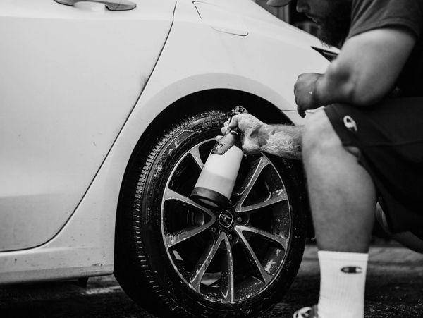 Man cleaning a car tire with a spray bottle and foam.