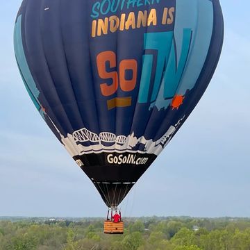 A hot air balloon with Southern Indiana branding flying over green trees.