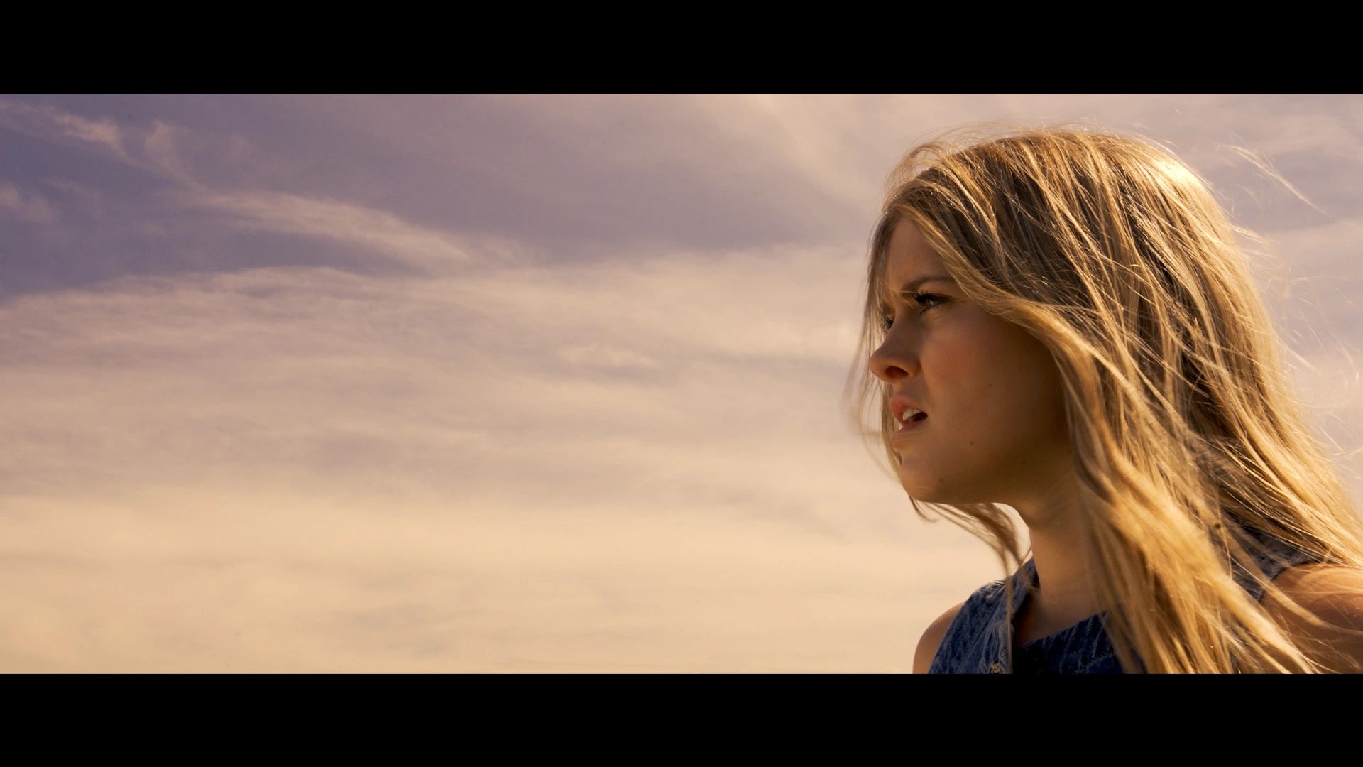 Young woman gazing thoughtfully into the distance under a cloudy sky.