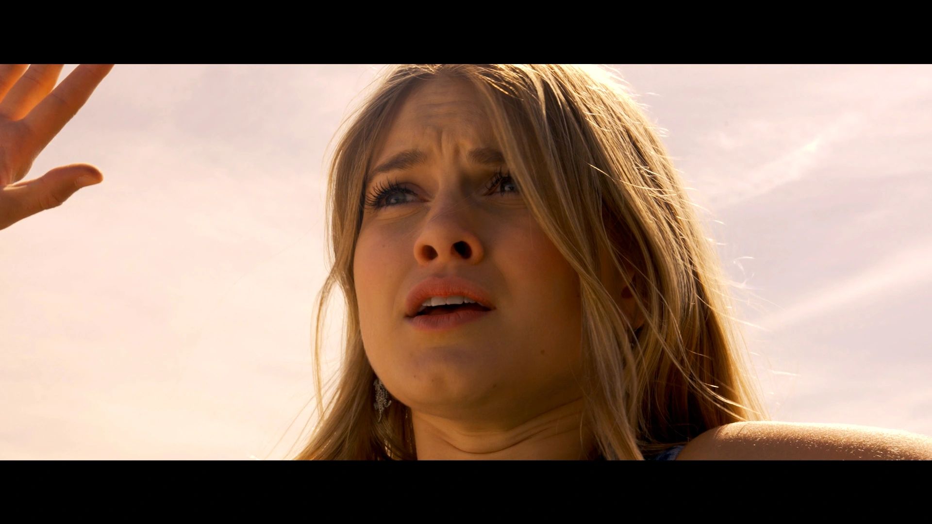 Close-up of a worried woman looking up with her hand raised against a bright sky.