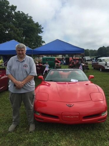 A picture of an old man standing next to a sports car