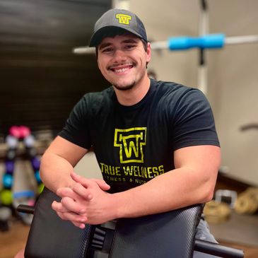 man wearing True Wellness t-shirt with hands crossed over gym equipment