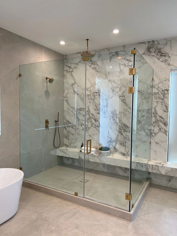 Corner shower for primary bathroom with brushed gold hardware and custom clear glass