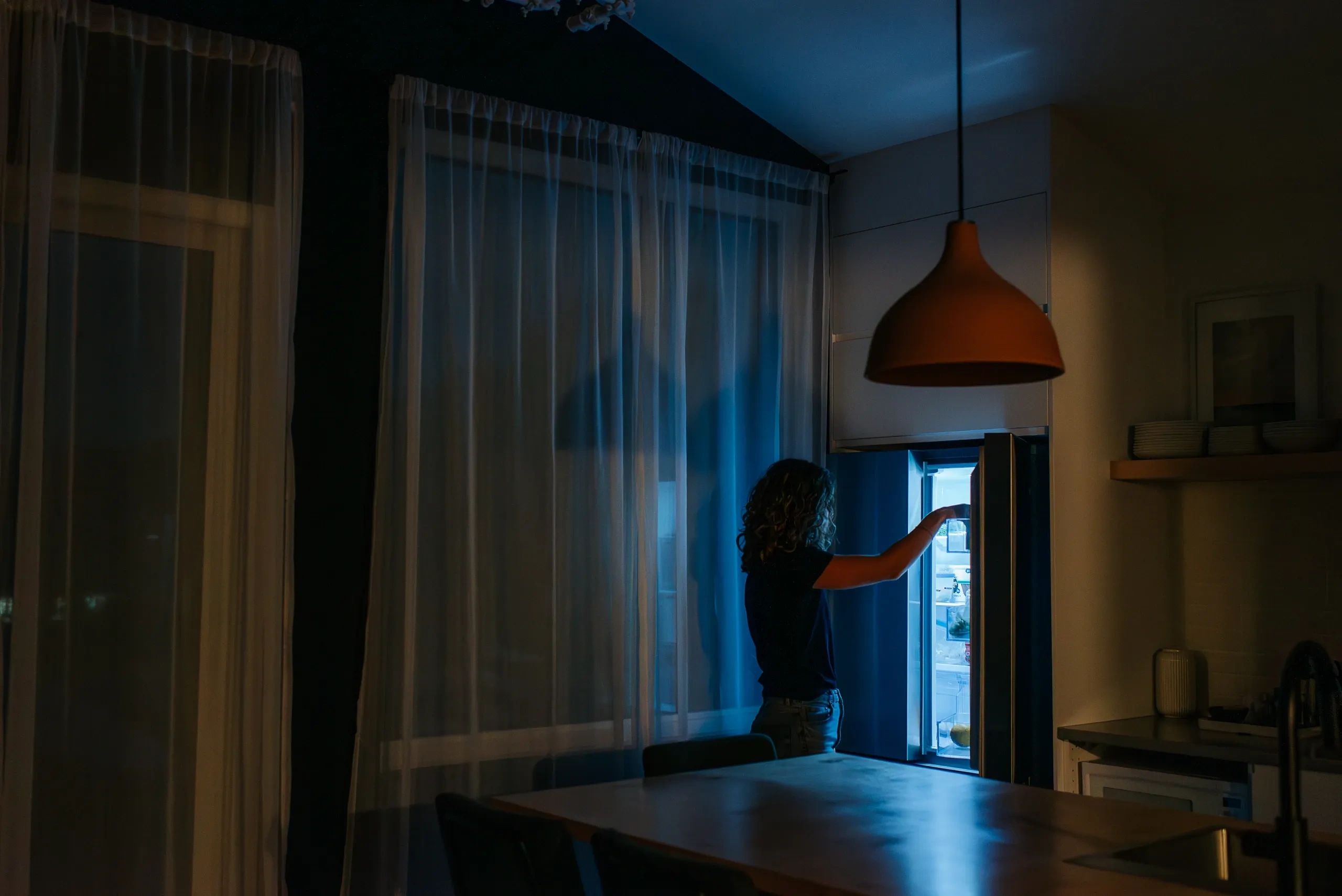 Person getting a late-night snack from the fridge in a dimly lit room.