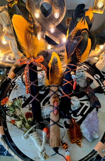 Three decorated sticks with orange and black feathers on a circular patterned background.