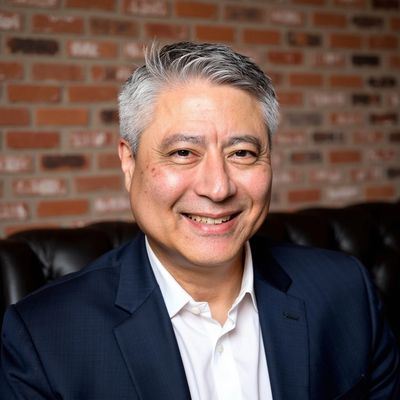 Smiling middle-aged man in a suit with a brick wall background.