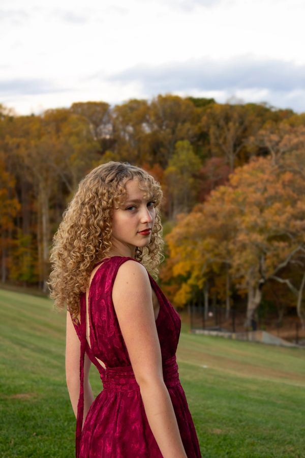 Woman in a red dress with curly hair standing outdoors in autumn.