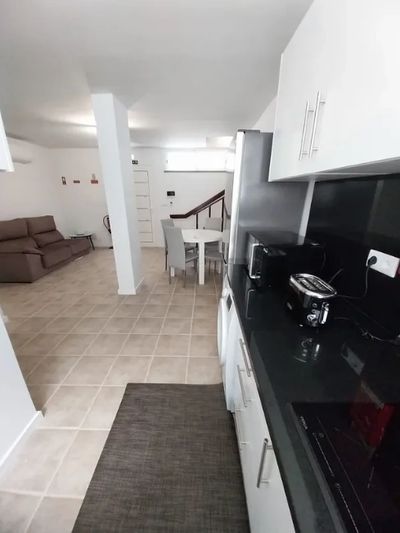 Modern open-plan kitchen and living area with white walls and tiled floors.
