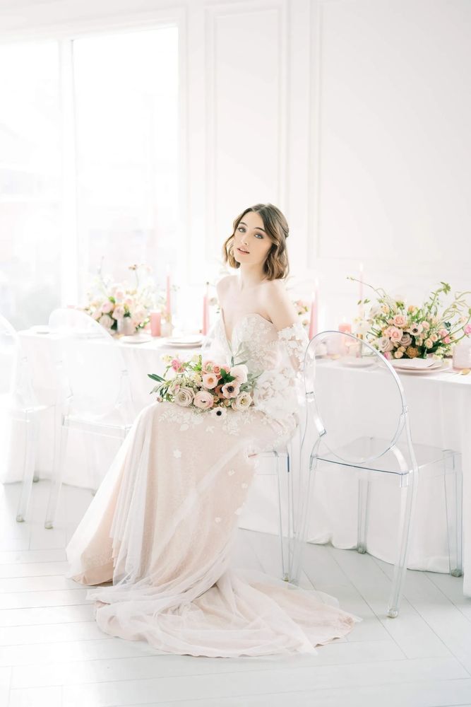 Bride in elegant white dress holding a bouquet, surrounded by greenery and candles.