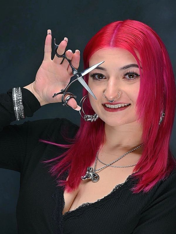 Smiling woman with bright pink hair holding scissors.