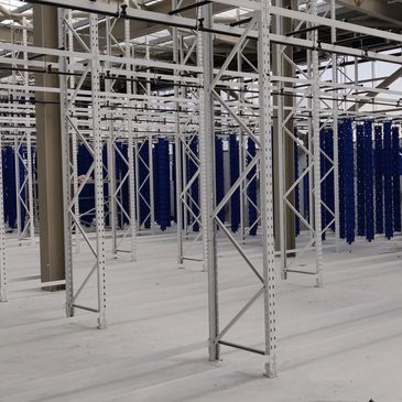 Empty industrial racks with blue hanging components in a spacious warehouse.