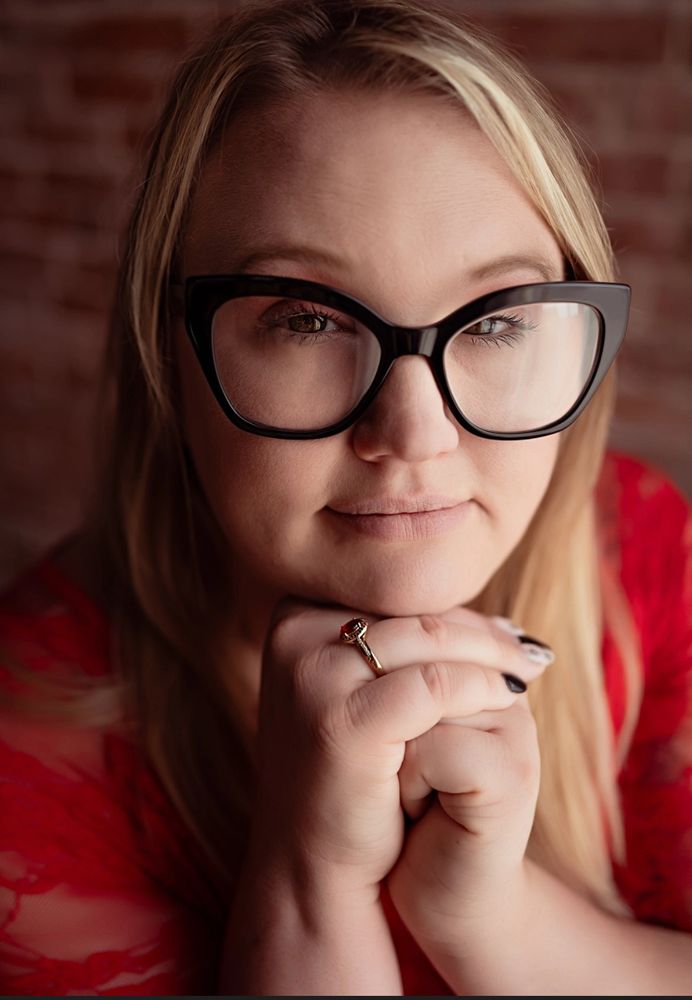 Close-up portrait of a woman with glasses wearing a red lace top.