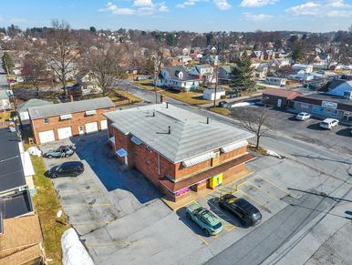 Aerial view of brick commercial building with parking lot and neighborhood houses.