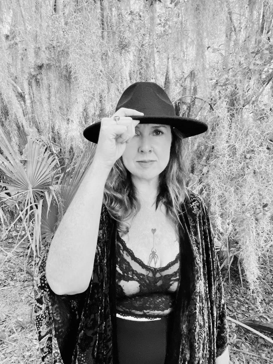 Woman in a black hat and lace top in a forest setting.