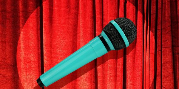 A turquoise microphone on a red stage curtain with a spotlight.