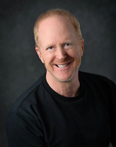 Smiling middle-aged man with red hair and beard wearing a black shirt.