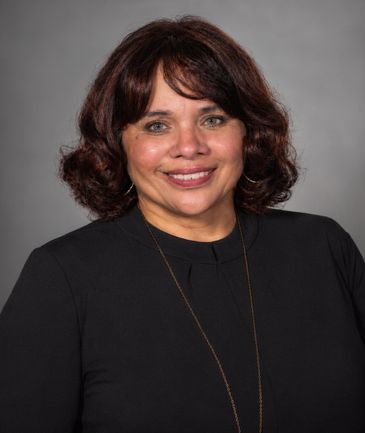 Smiling woman with medium-length dark hair in a black top against a gray background.