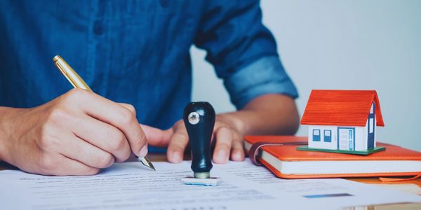 Signing a document with a gold pen, alongside a notary stamp and a model house.